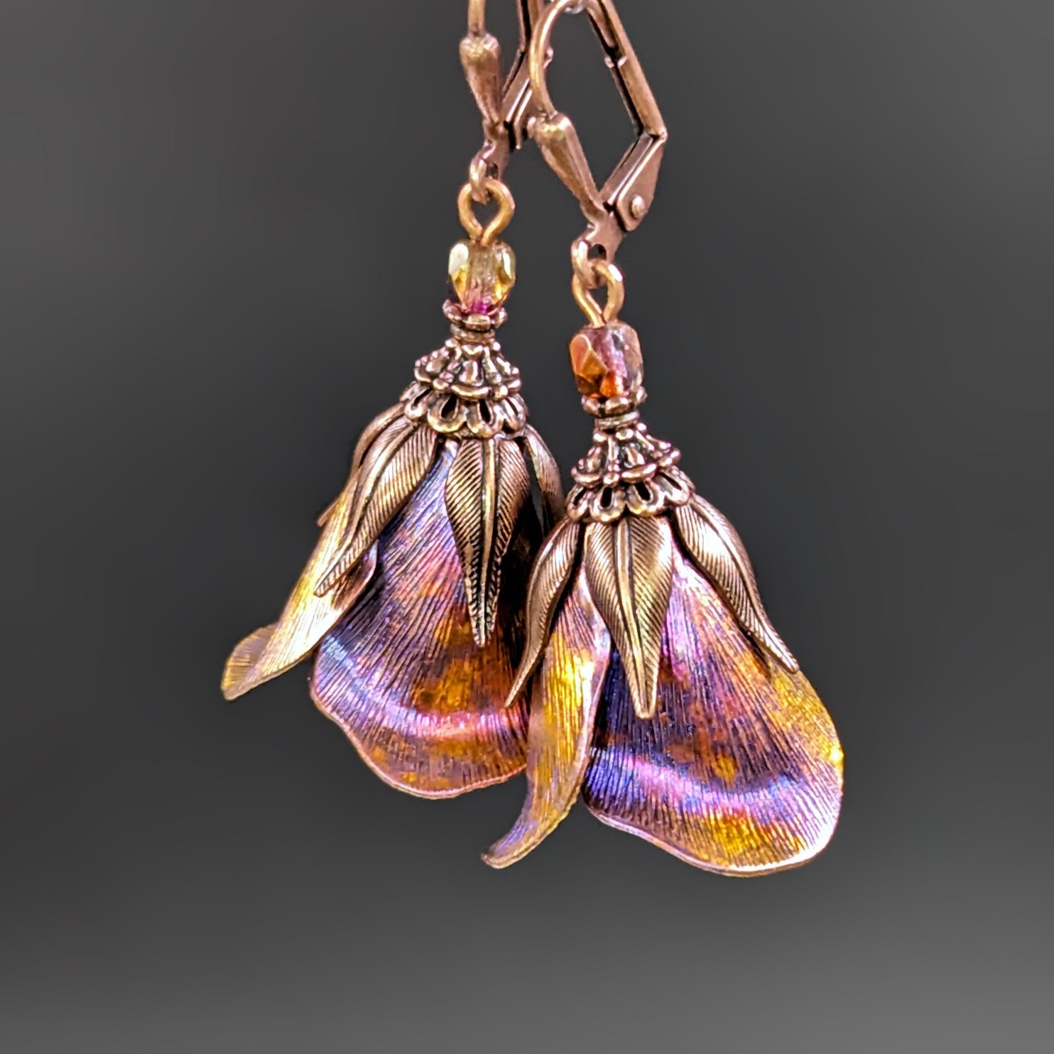 Iridescent Flower Earrings in Pink, Orange, Yellow, and blue with Antiqued Copper metal. The flower earrings are photographed on a black background.
